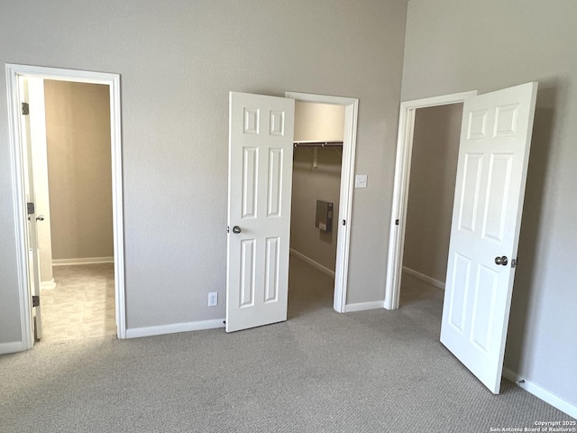 unfurnished bedroom featuring carpet floors, a spacious closet, a closet, and baseboards