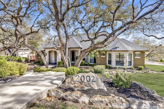 french country style house featuring roof with shingles, a front lawn, and stucco siding