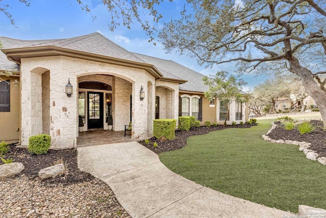 view of front of house featuring stone siding, a shingled roof, and a front yard