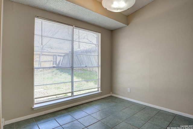 tiled empty room with baseboards and a textured ceiling