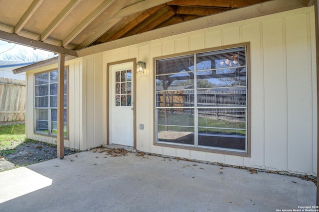 entrance to property with board and batten siding, a patio area, and fence