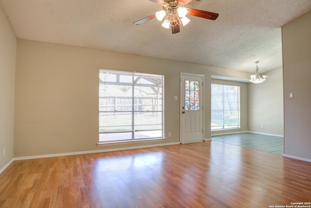 empty room featuring a textured ceiling, baseboards, wood finished floors, and ceiling fan with notable chandelier