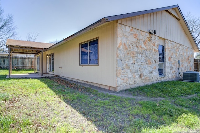 view of property exterior with stone siding, fence, central AC, and a yard