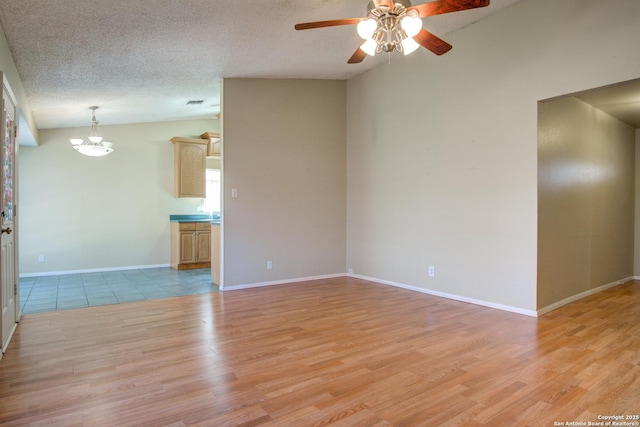 spare room featuring lofted ceiling, light wood-type flooring, baseboards, and a textured ceiling