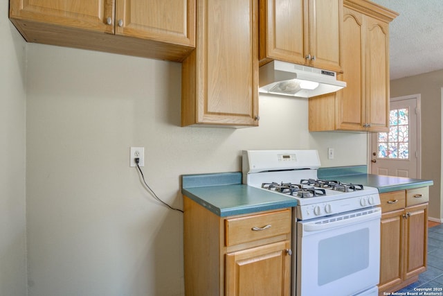 kitchen with a textured ceiling, under cabinet range hood, white gas range oven, light brown cabinetry, and dark countertops