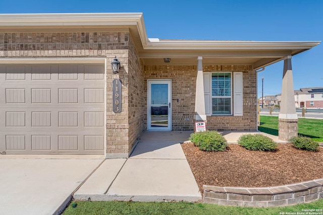 property entrance with a garage, a porch, and brick siding