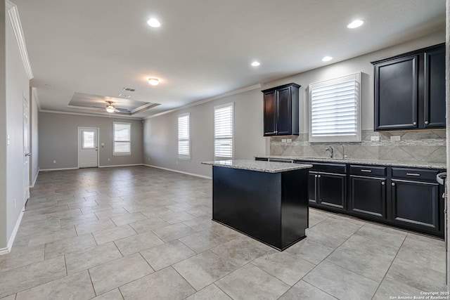 kitchen with a center island, tasteful backsplash, a raised ceiling, ornamental molding, and a ceiling fan