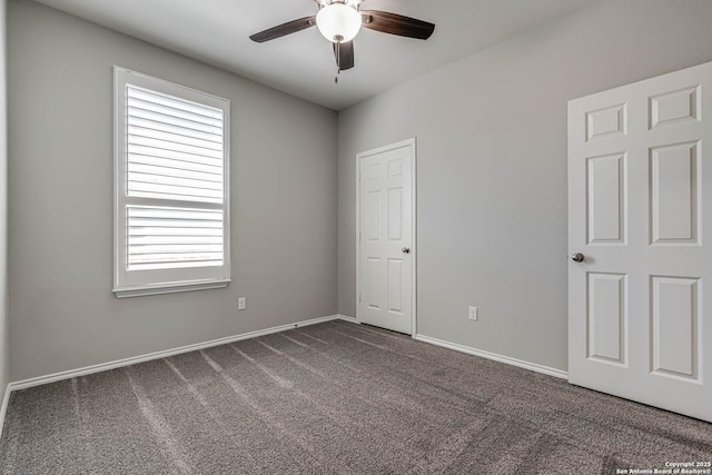 empty room with a ceiling fan, dark colored carpet, and baseboards