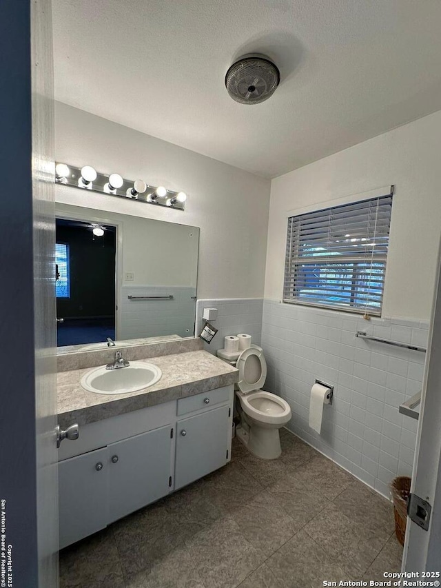 bathroom with toilet, a wainscoted wall, a textured ceiling, vanity, and tile walls