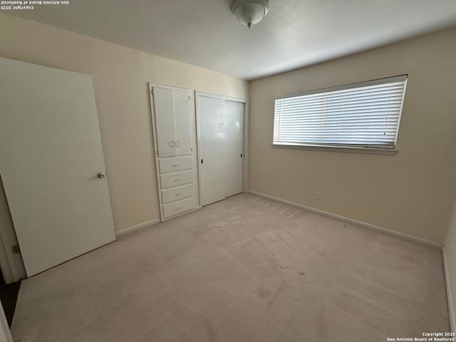 unfurnished bedroom with light carpet, a closet, and baseboards