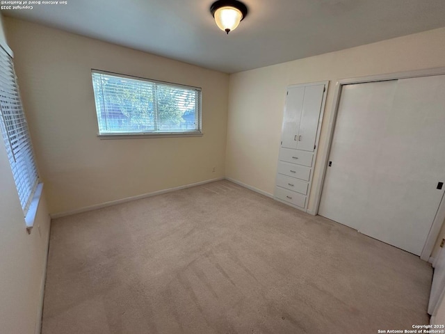 unfurnished bedroom featuring a closet, light carpet, and baseboards