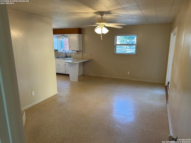 unfurnished living room featuring ceiling fan, baseboards, and a sink