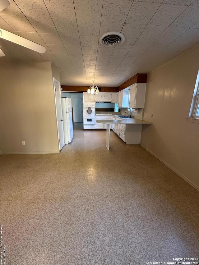 kitchen with baseboards, visible vents, freestanding refrigerator, a peninsula, and a kitchen bar