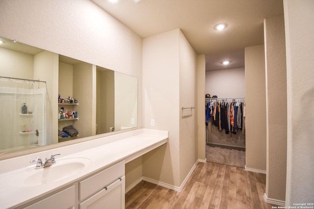 full bathroom featuring a walk in closet, curtained shower, vanity, wood finished floors, and baseboards