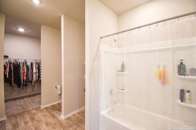 bathroom with recessed lighting, wood finished floors, baseboards, shower / bathing tub combination, and a walk in closet