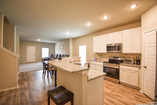 kitchen with light stone counters, stainless steel appliances, recessed lighting, open floor plan, and a kitchen bar