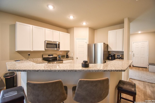 kitchen with appliances with stainless steel finishes, white cabinets, a breakfast bar area, and recessed lighting