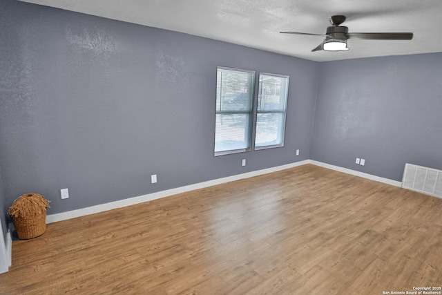 spare room with a ceiling fan, wood finished floors, visible vents, and baseboards