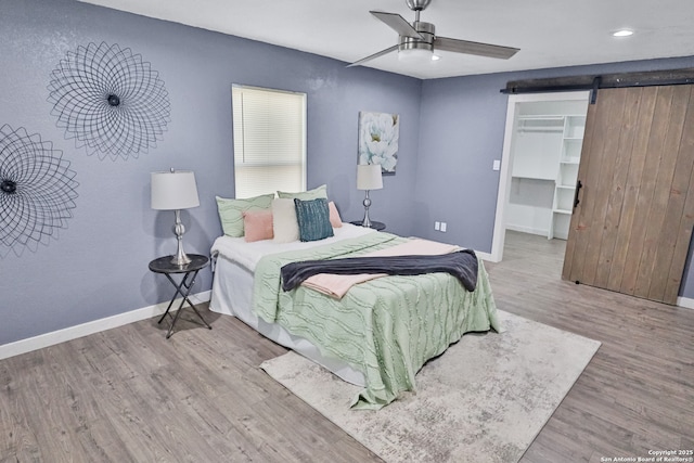 bedroom with a walk in closet, wood finished floors, baseboards, and a barn door