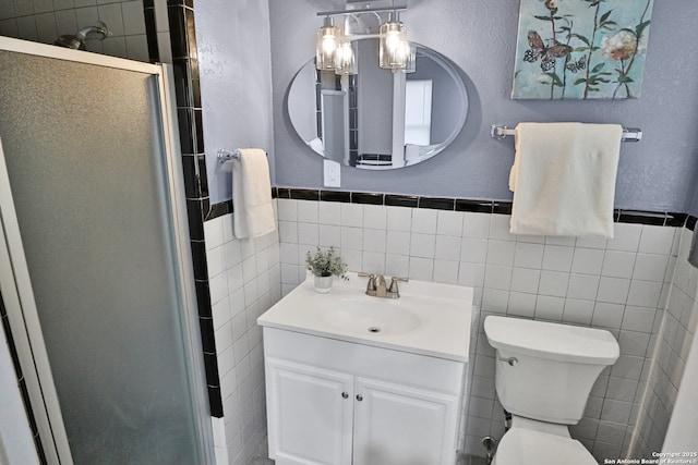 bathroom with a stall shower, a textured wall, toilet, vanity, and tile walls