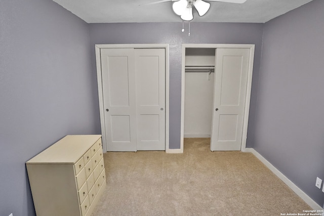 unfurnished bedroom with two closets, baseboards, a ceiling fan, and light colored carpet