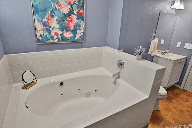 bathroom with a textured wall, toilet, a tub with jets, tile patterned floors, and vanity