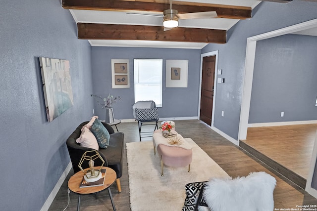 living area featuring beam ceiling, baseboards, and wood finished floors