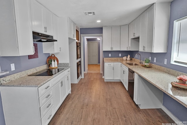 kitchen featuring light wood-style flooring, under cabinet range hood, a sink, visible vents, and black appliances