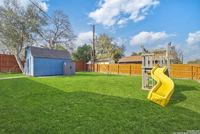 view of yard with a storage shed, a playground, a fenced backyard, and an outbuilding