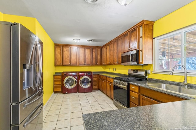 kitchen with washing machine and clothes dryer, light tile patterned floors, dark countertops, appliances with stainless steel finishes, and a sink