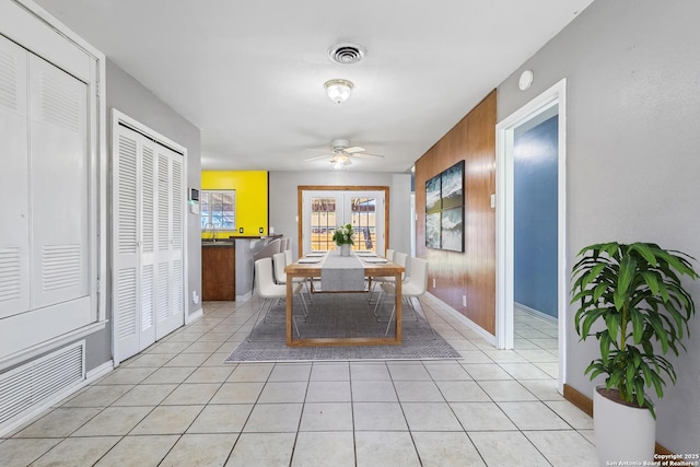 dining room with light tile patterned floors, a ceiling fan, visible vents, and wooden walls