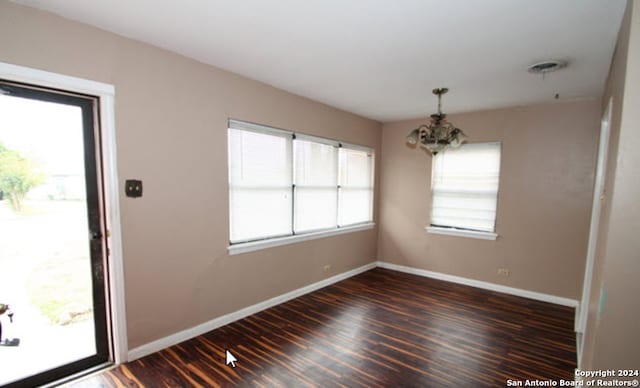 unfurnished room with baseboards, dark wood-type flooring, and an inviting chandelier