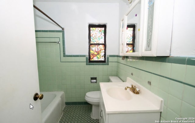 full bath with tile walls, shower / bathing tub combination, toilet, wainscoting, and vanity