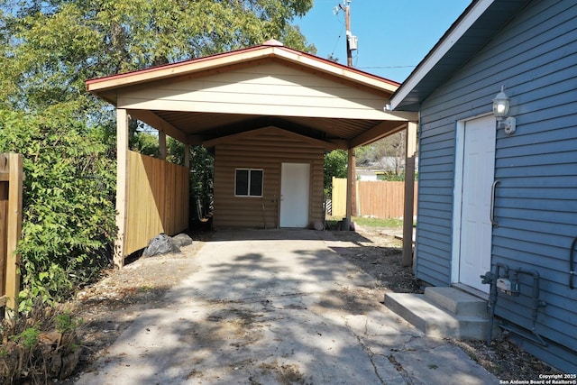 exterior space featuring entry steps, concrete driveway, fence, and an outdoor structure