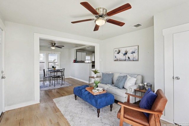 living room featuring visible vents, light wood-style flooring, a ceiling fan, and baseboards