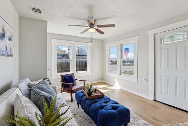 living room with visible vents, baseboards, ceiling fan, light wood-style floors, and a textured ceiling