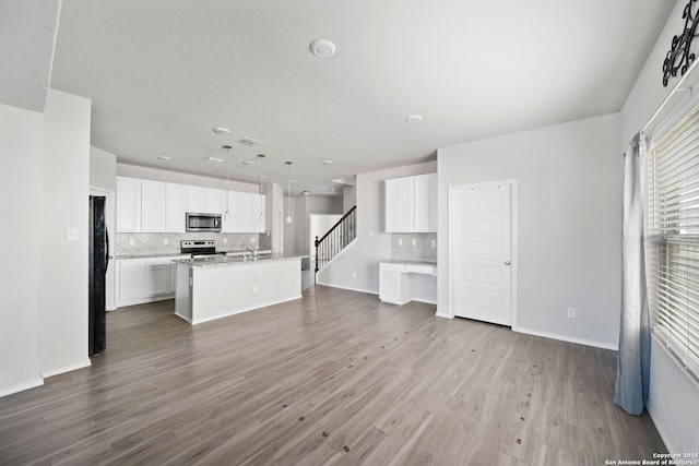 unfurnished living room with dark wood-style floors, visible vents, stairway, a sink, and baseboards