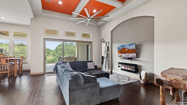 living area featuring ceiling fan, dark wood-style flooring, coffered ceiling, baseboards, and a glass covered fireplace