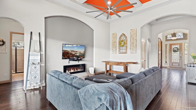 living area featuring a high ceiling, dark wood-style flooring, coffered ceiling, baseboards, and a glass covered fireplace