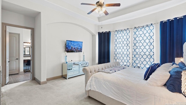 carpeted bedroom with baseboards, a tray ceiling, and a ceiling fan