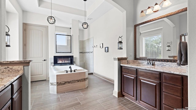 bathroom featuring a walk in shower, vanity, baseboards, a bath, and a glass covered fireplace