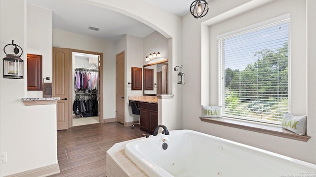 bathroom with visible vents, vanity, baseboards, a jetted tub, and a walk in closet