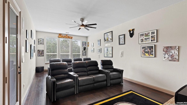 cinema room with dark wood-style floors, a ceiling fan, and baseboards