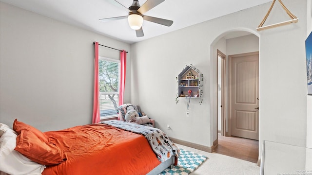 bedroom featuring baseboards, arched walkways, a ceiling fan, and wood finished floors