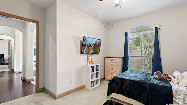 carpeted bedroom with a ceiling fan, arched walkways, and baseboards