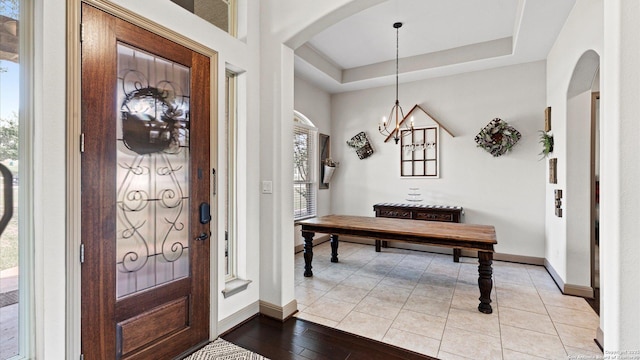 foyer featuring arched walkways, a tray ceiling, light tile patterned flooring, and baseboards