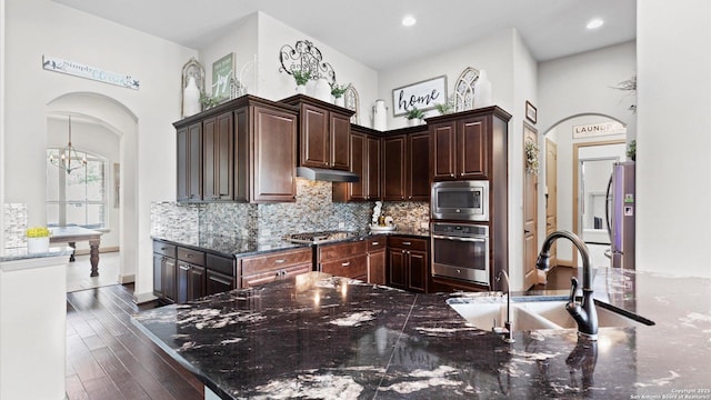 kitchen featuring arched walkways, under cabinet range hood, stainless steel appliances, a sink, and backsplash