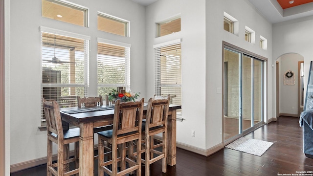 dining room featuring arched walkways, dark wood-style flooring, a towering ceiling, and baseboards