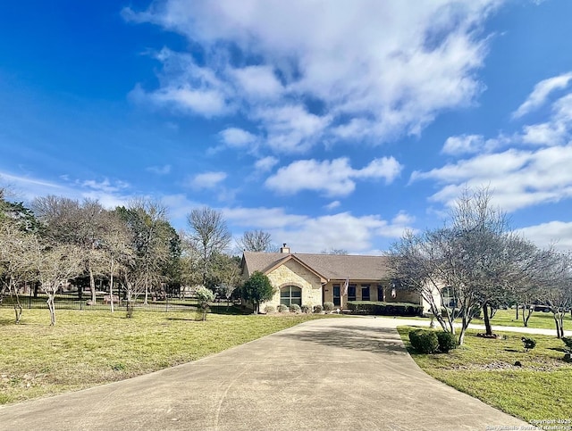 view of front of property featuring stone siding, a front yard, concrete driveway, and a chimney