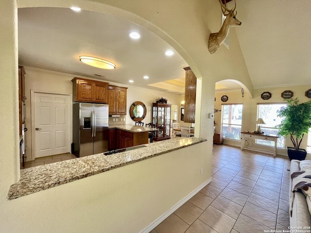 kitchen featuring arched walkways, a peninsula, stainless steel refrigerator with ice dispenser, and light stone countertops